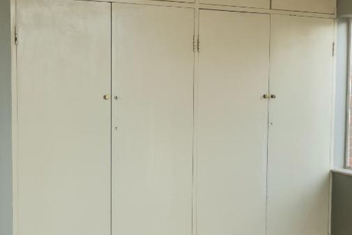 A bedroom featuring extensive built-in floor-to-ceiling cupboards with overhead storage and traditional parquet flooring.