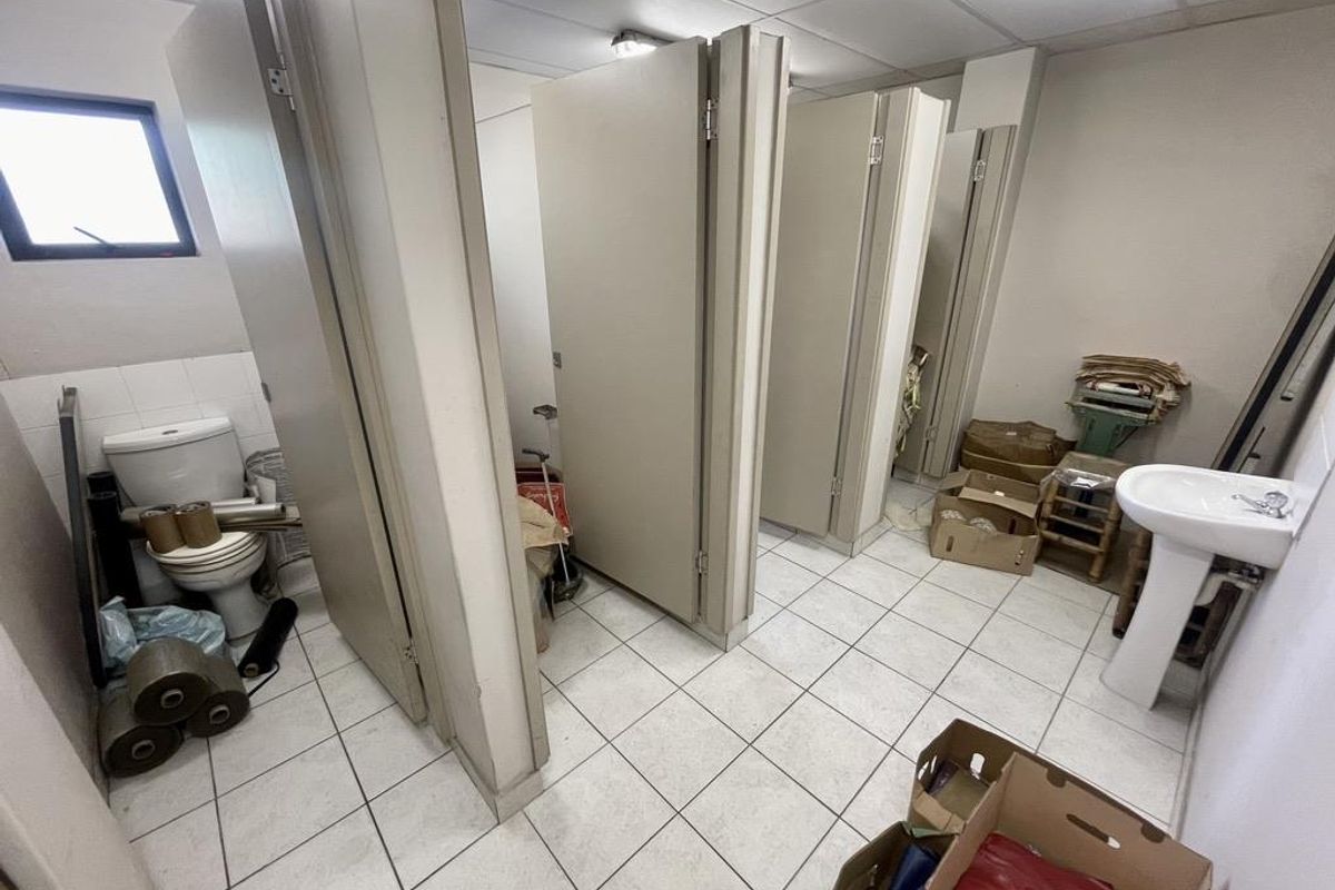 Industrial restroom facility featuring multiple partitioned toilet stalls and a pedestal sink with tiled flooring and drop ceiling.