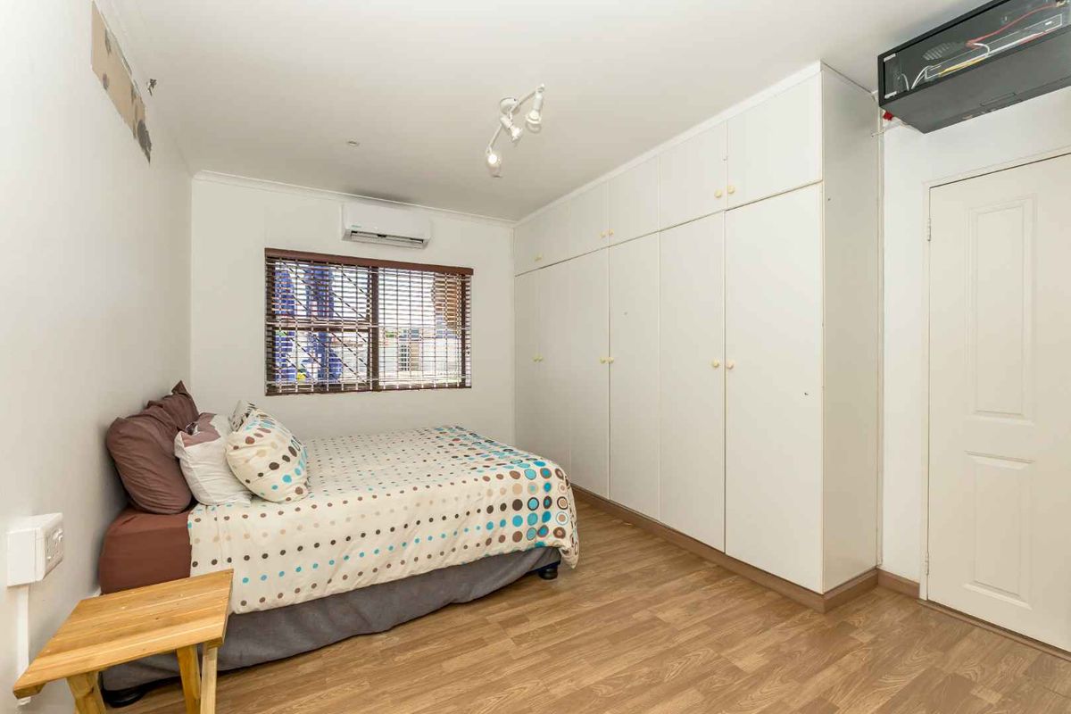 A bedroom featuring built-in floor-to-ceiling wardrobes, wood-look laminate flooring, and a wall-mounted air conditioning unit.
