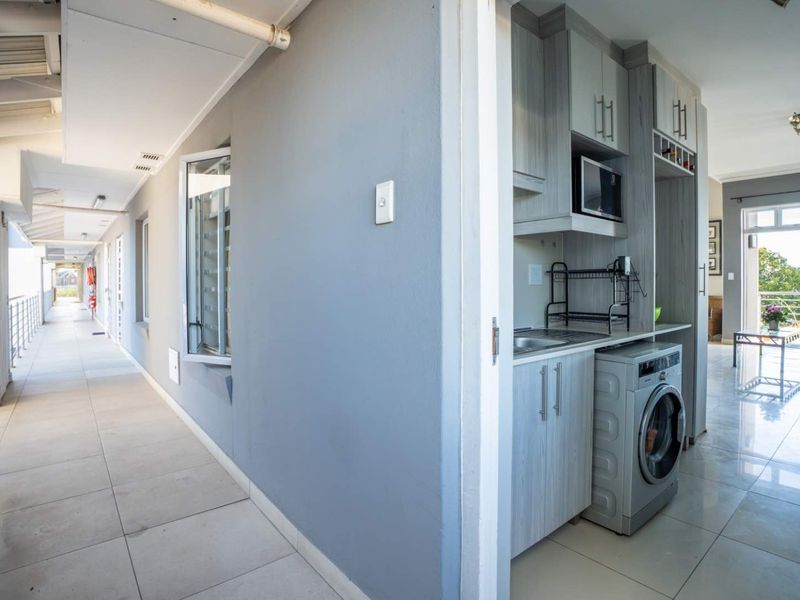 A functional laundry area featuring built-in cabinetry and a sink, conveniently located adjacent to an external apartment walkway.