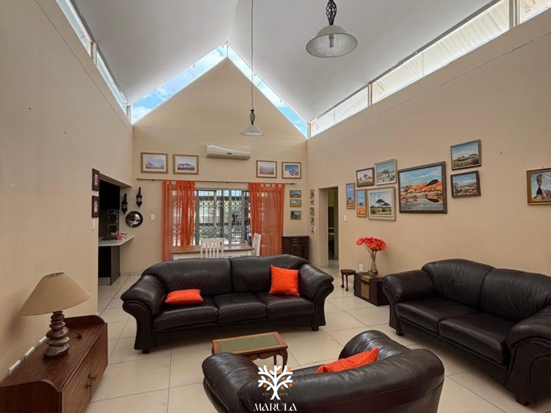 Spacious living room featuring a high vaulted ceiling with clerestory windows, tiled flooring, and a wall-mounted split-system air conditioner.