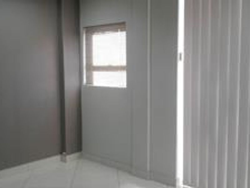 A clean, empty office space featuring neutral grey walls, tiled flooring, and vertical blinds on the window.