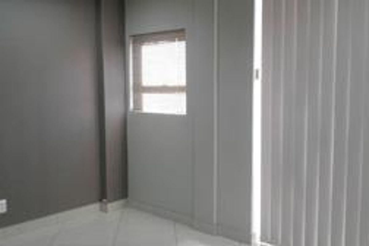 A clean, empty office space featuring neutral grey walls, tiled flooring, and vertical blinds on the window.