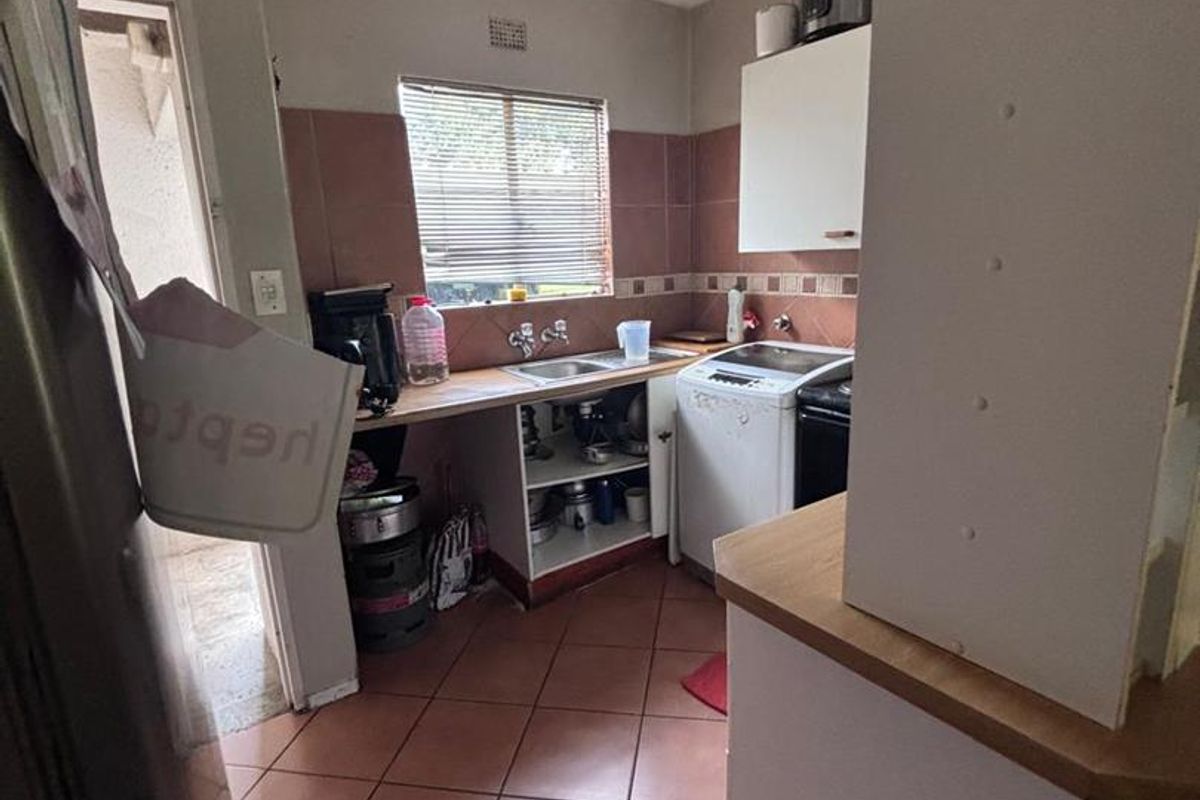 A compact kitchen featuring tiled flooring, tiled splashbacks, and basic cabinetry with an integrated sink and space for laundry appliances.