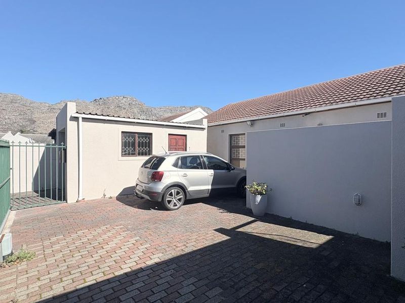Front exterior view of the property featuring a paved driveway, secure metal gate, and mountain views in the background.