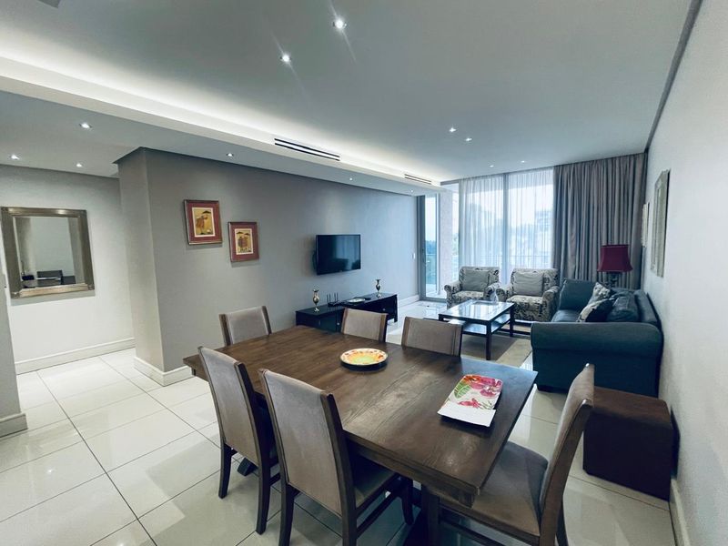 A spacious open-plan living and dining area featuring modern tiled floors, recessed ceiling lighting, and large sliding glass doors leading to a balcony.