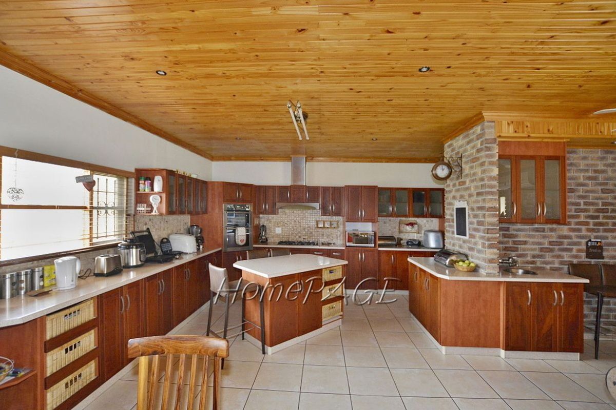 Spacious kitchen featuring timber cabinetry, a central island, stone countertops, and a distinctive exposed brick feature wall with a timber-clad ceiling.