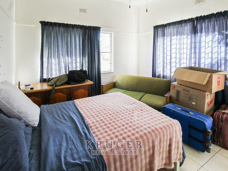 A functional bedroom featuring tiled flooring, neutral walls, and large windows with curtain rails, offering a blank canvas for personalization.