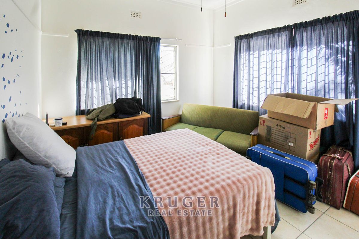 A functional bedroom featuring tiled flooring, neutral walls, and large windows with curtain rails, offering a blank canvas for personalization.