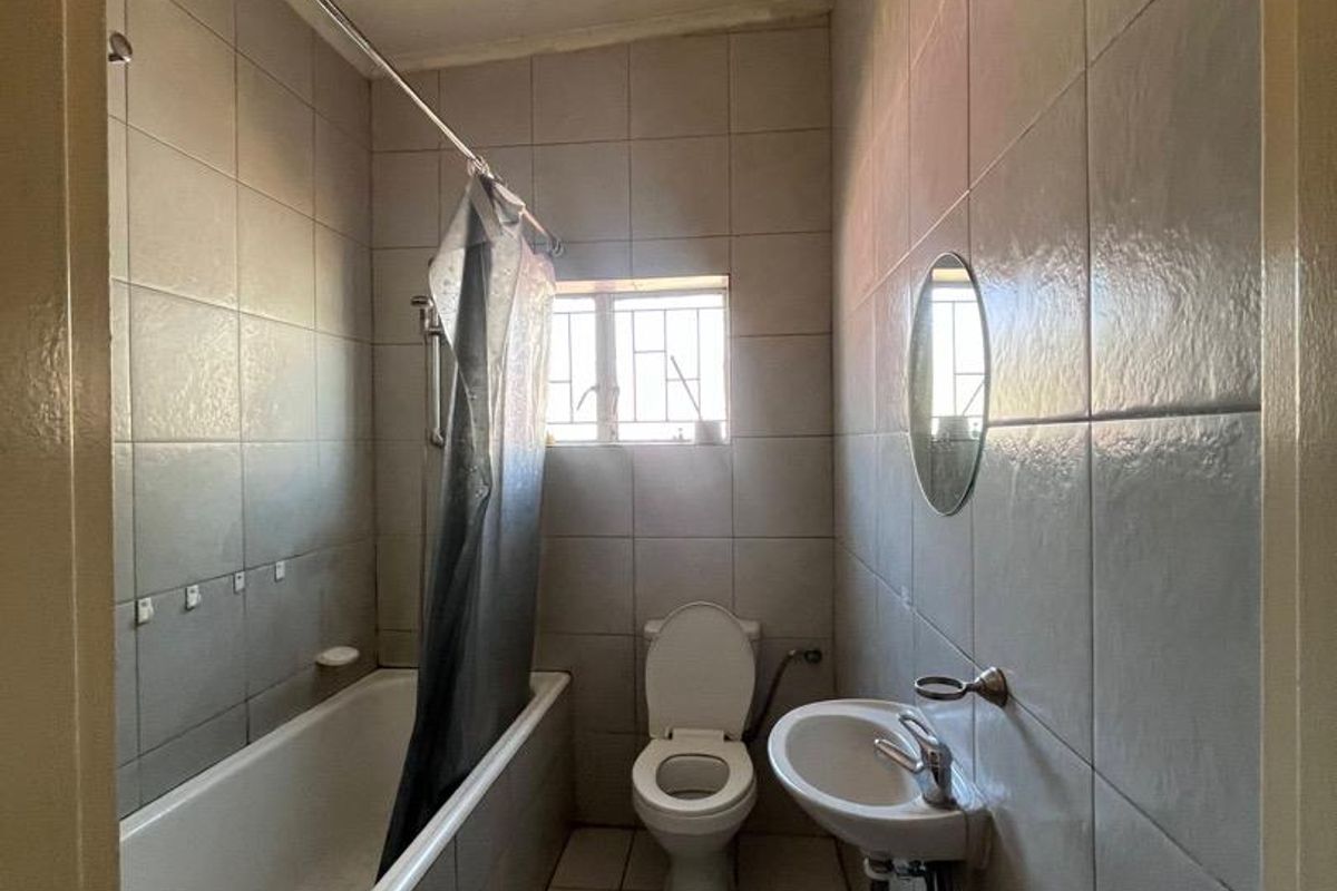 A functional bathroom featuring a bathtub, wall-mounted basin, and toilet with full-height wall tiling and security bars on the window.