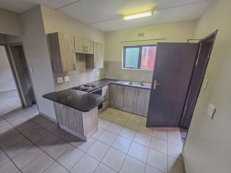 A functional kitchen featuring wood-look cabinetry, granite countertops, a built-in hob and oven, and tiled flooring throughout.