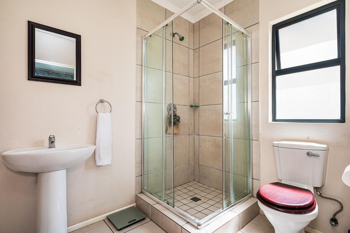 A functional bathroom featuring a pedestal basin, a glass-enclosed shower with tiled walls, and a standard toilet.