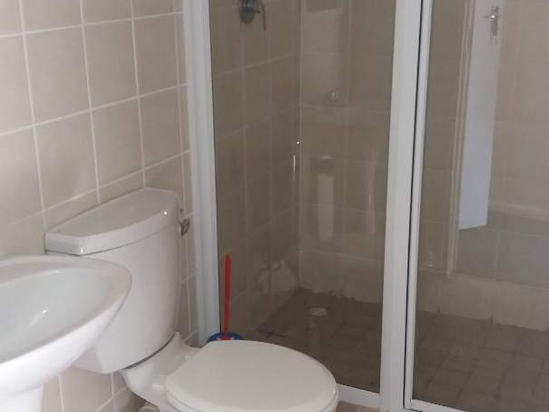 A functional bathroom featuring a pedestal basin, toilet, and a glass-enclosed shower with neutral wall and floor tiling.