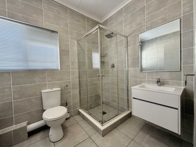 A modern, well-maintained bathroom featuring a glass shower enclosure, wall-mounted vanity, and neutral floor-to-ceiling tiling.