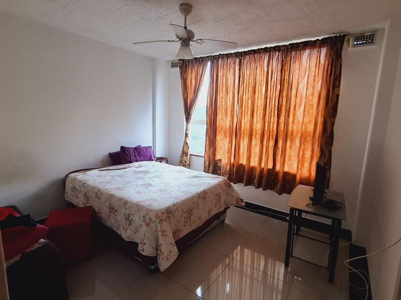 A bedroom featuring tiled flooring, a ceiling fan, and large windows with curtains, offering a functional space with potential for modern updates.