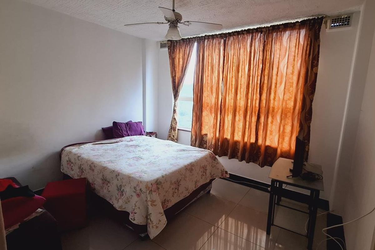 A bedroom featuring tiled flooring, a ceiling fan, and large windows with curtains, offering a functional space with potential for modern updates.