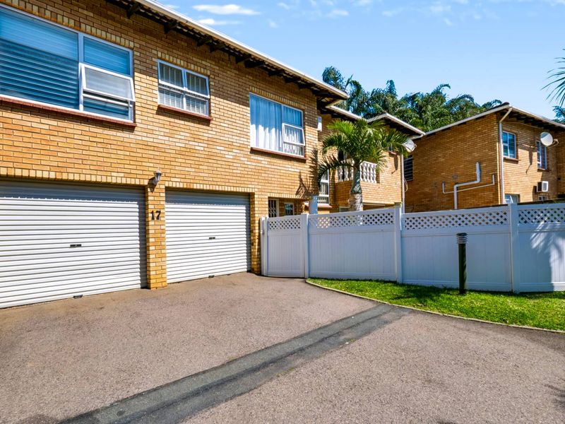 Front exterior view of a townhouse featuring a double garage with roller shutter doors, brick facade, and a private fenced entrance area.