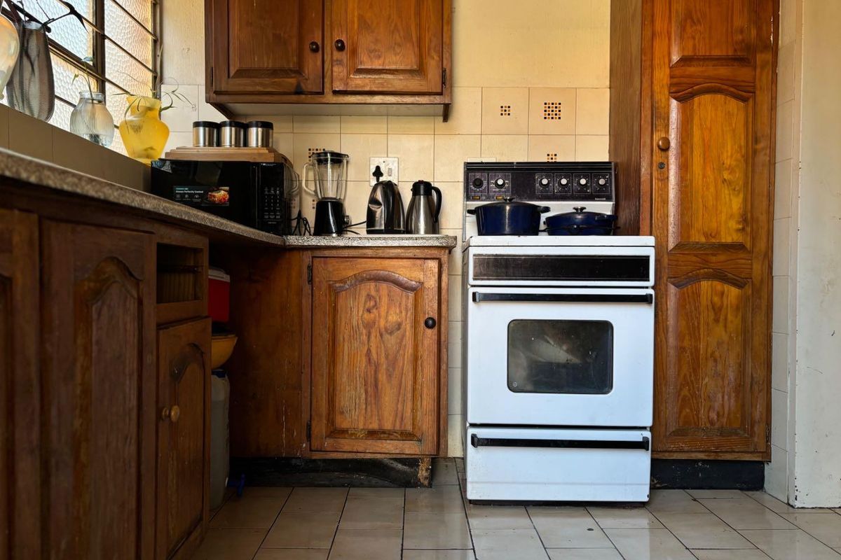 A dated kitchen featuring traditional wooden cabinetry, tiled backsplash, and a freestanding oven, offering significant potential for a modern renovation.