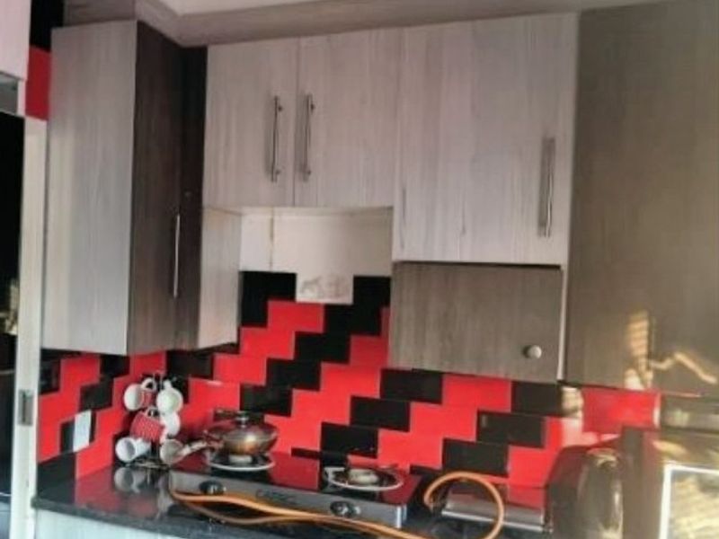 A kitchen area featuring built-in cabinetry, a gas hob, and a distinctive red and black tiled splashback, requiring minor repairs to cabinetry.