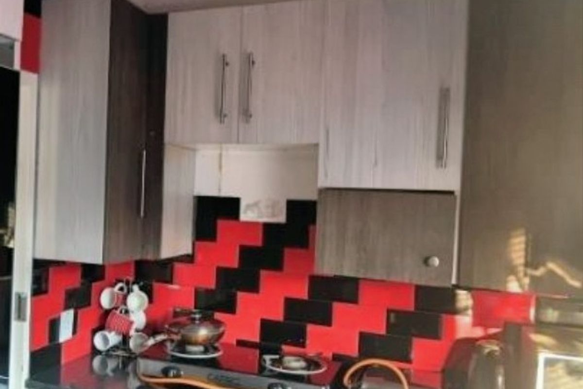 A kitchen area featuring built-in cabinetry, a gas hob, and a distinctive red and black tiled splashback, requiring minor repairs to cabinetry.