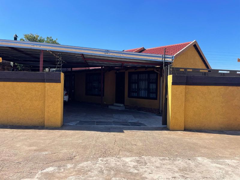 Front exterior view of the house featuring a covered carport, security gates, and a boundary wall with a concrete driveway.