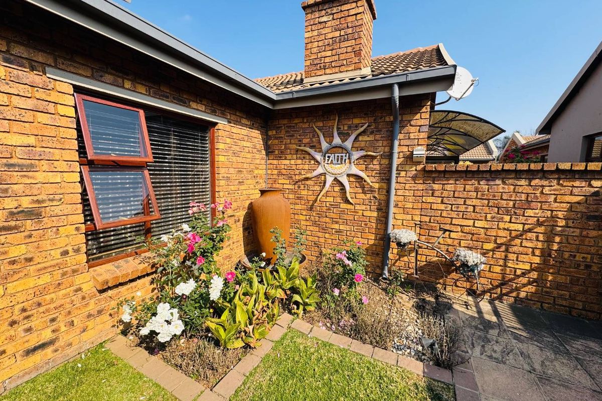 A private rear garden area featuring face-brick exterior walls, a brick chimney stack, paved pathways, and established garden beds.