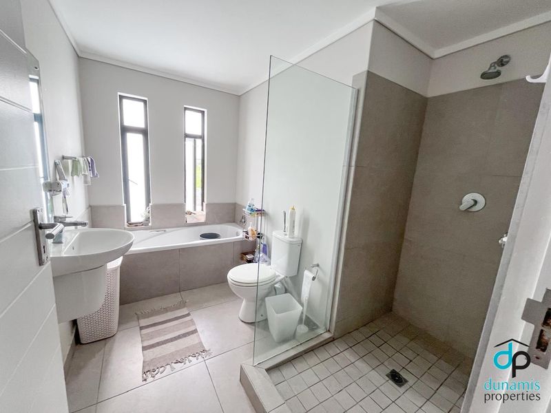 Modern bathroom featuring a pedestal basin, toilet, built-in bathtub, and a separate walk-in shower with a glass screen and neutral tiling.