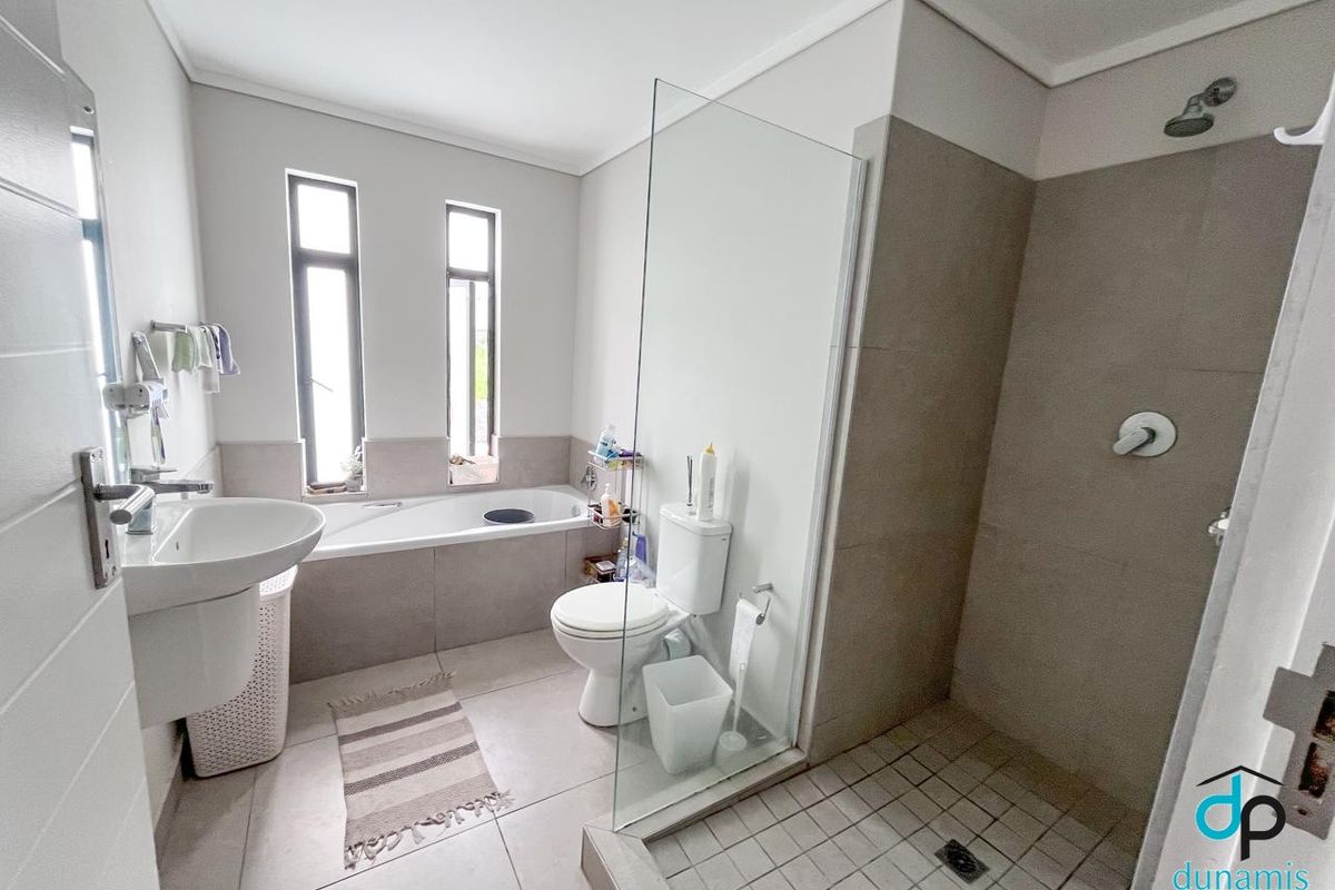 Modern bathroom featuring a pedestal basin, toilet, built-in bathtub, and a separate walk-in shower with a glass screen and neutral tiling.