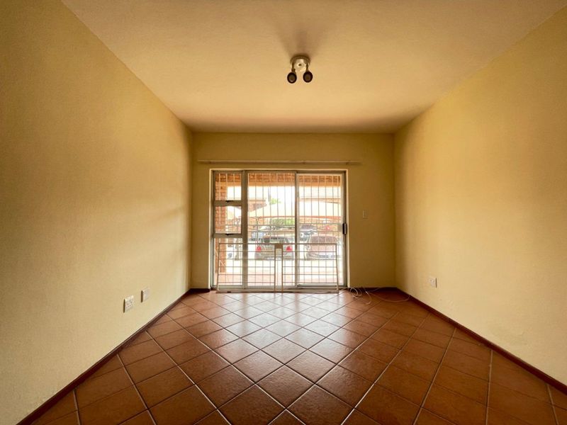 An empty living room featuring tiled flooring and a sliding glass door with an integrated security gate, providing access to the exterior.