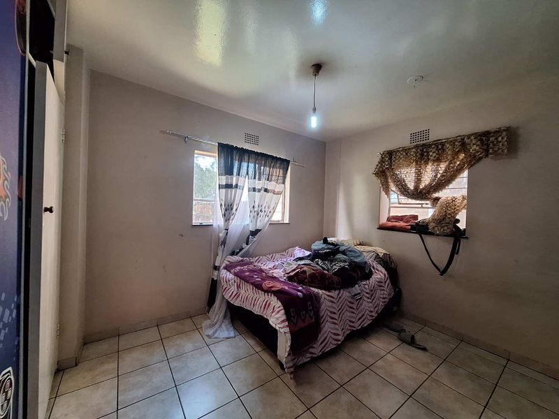 A bedroom featuring tiled flooring, two windows with security vents, and a simple pendant light fixture.