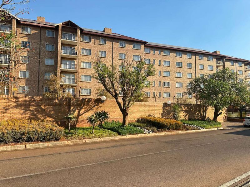 Exterior view of a multi-story brick apartment complex featuring private balconies, a perimeter wall, and solar panel installations on the roof.