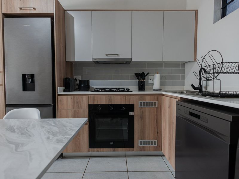 Modern kitchen featuring wood-grain cabinetry, stone countertops, subway tile backsplash, and integrated appliances including a gas hob and oven.
