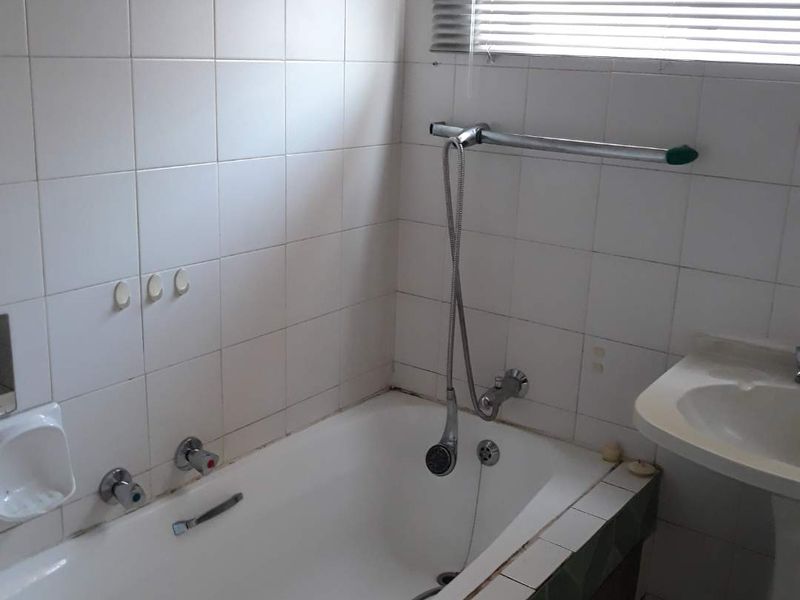 A dated bathroom featuring a standard bathtub, pedestal basin, and wall tiling. The space requires cosmetic updates to improve its overall condition and appeal.