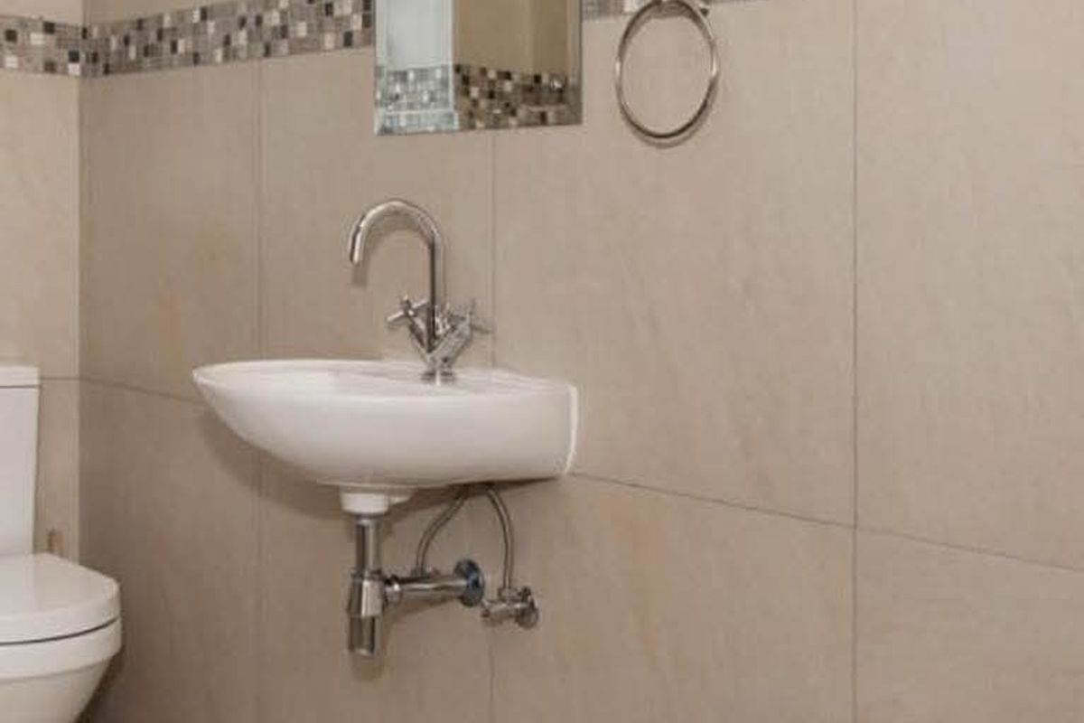 A compact bathroom featuring neutral wall tiles with a decorative mosaic border, a wall-mounted basin, and a modern chrome faucet.