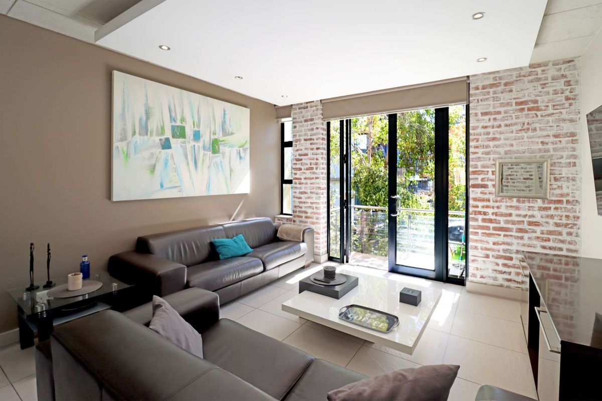 Modern living room featuring exposed brick feature wall, recessed ceiling lighting, and large glass sliding doors opening onto a private balcony.