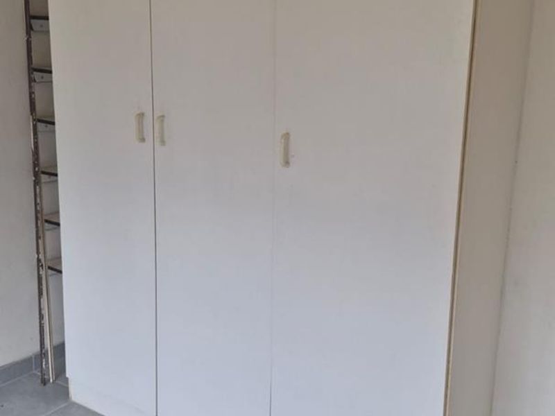 A bedroom featuring neutral tiled flooring and a large white built-in wardrobe with three doors.