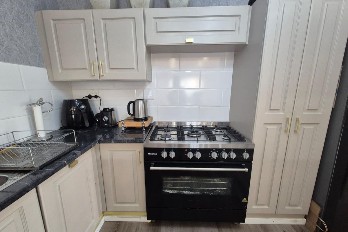 A compact kitchen featuring shaker-style cabinetry, a subway tile backsplash, dark stone-look countertops, and a built-in gas oven and hob.