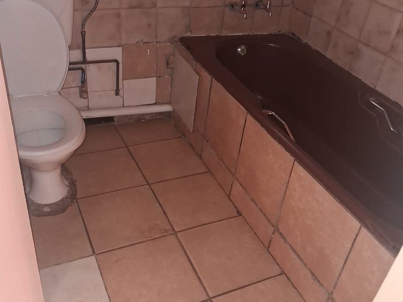 A dated bathroom featuring a bathtub and toilet with visible wall and floor tiling, requiring renovation and cosmetic updates to improve functionality and aesthetics.