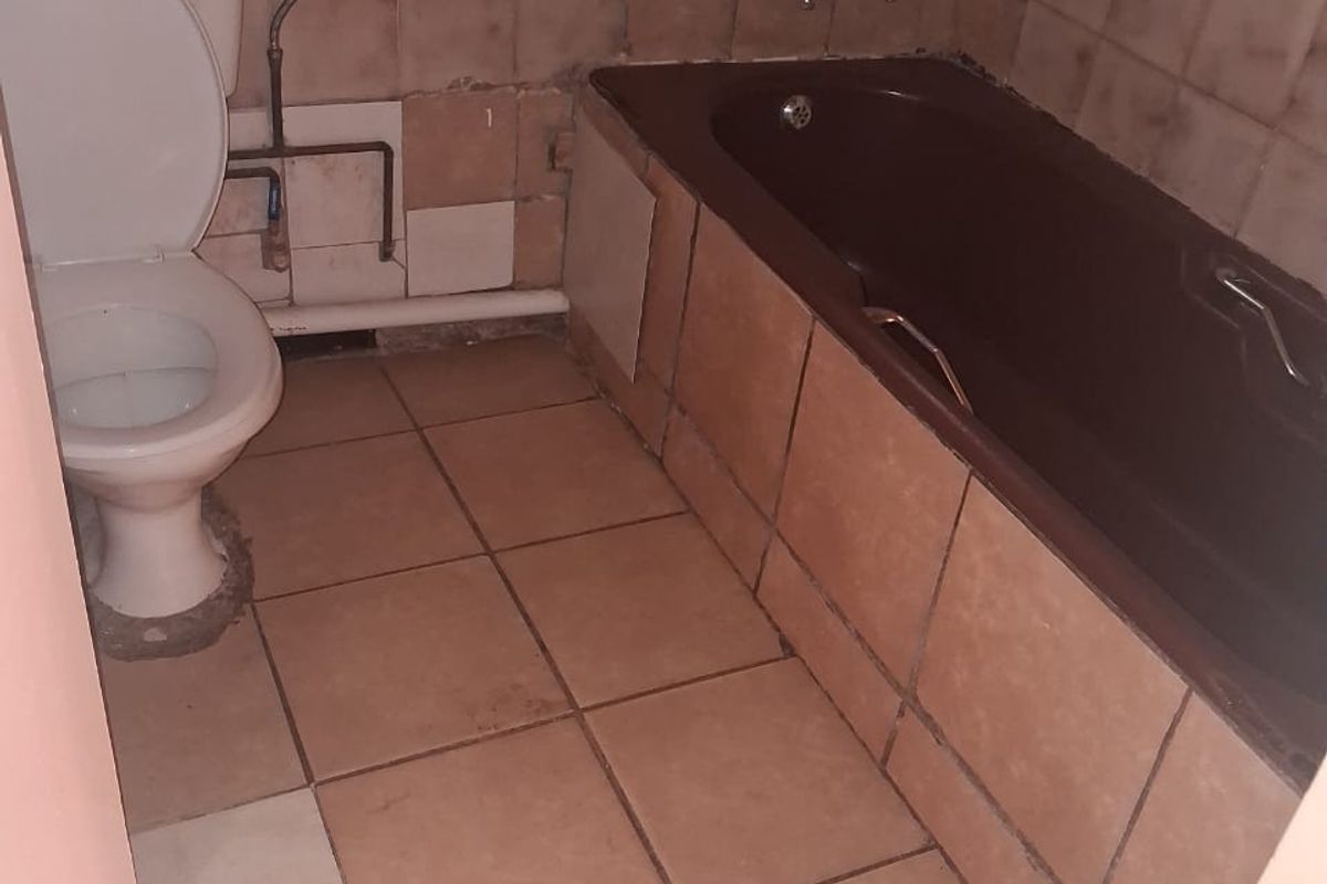 A dated bathroom featuring a bathtub and toilet with visible wall and floor tiling, requiring renovation and cosmetic updates to improve functionality and aesthetics.