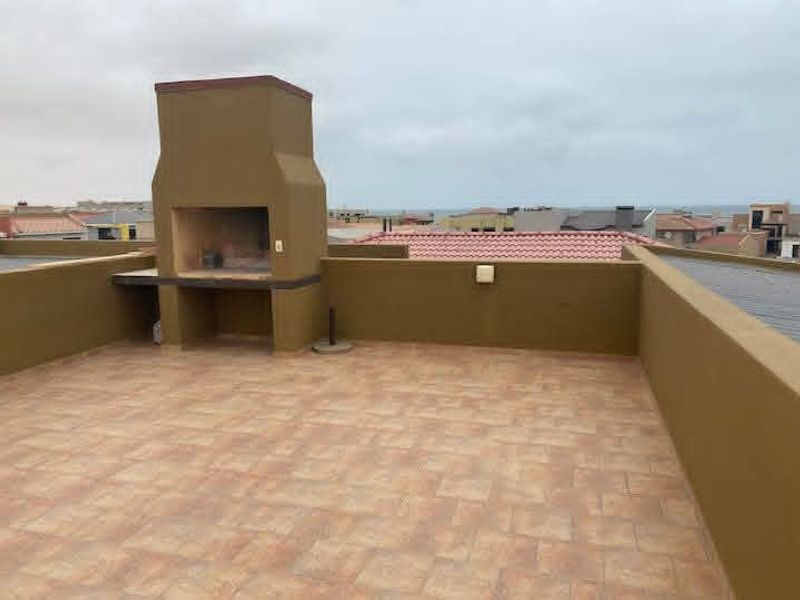 An open-air rooftop patio featuring a built-in braai, tiled flooring, and perimeter walls, offering an elevated outdoor entertainment space.