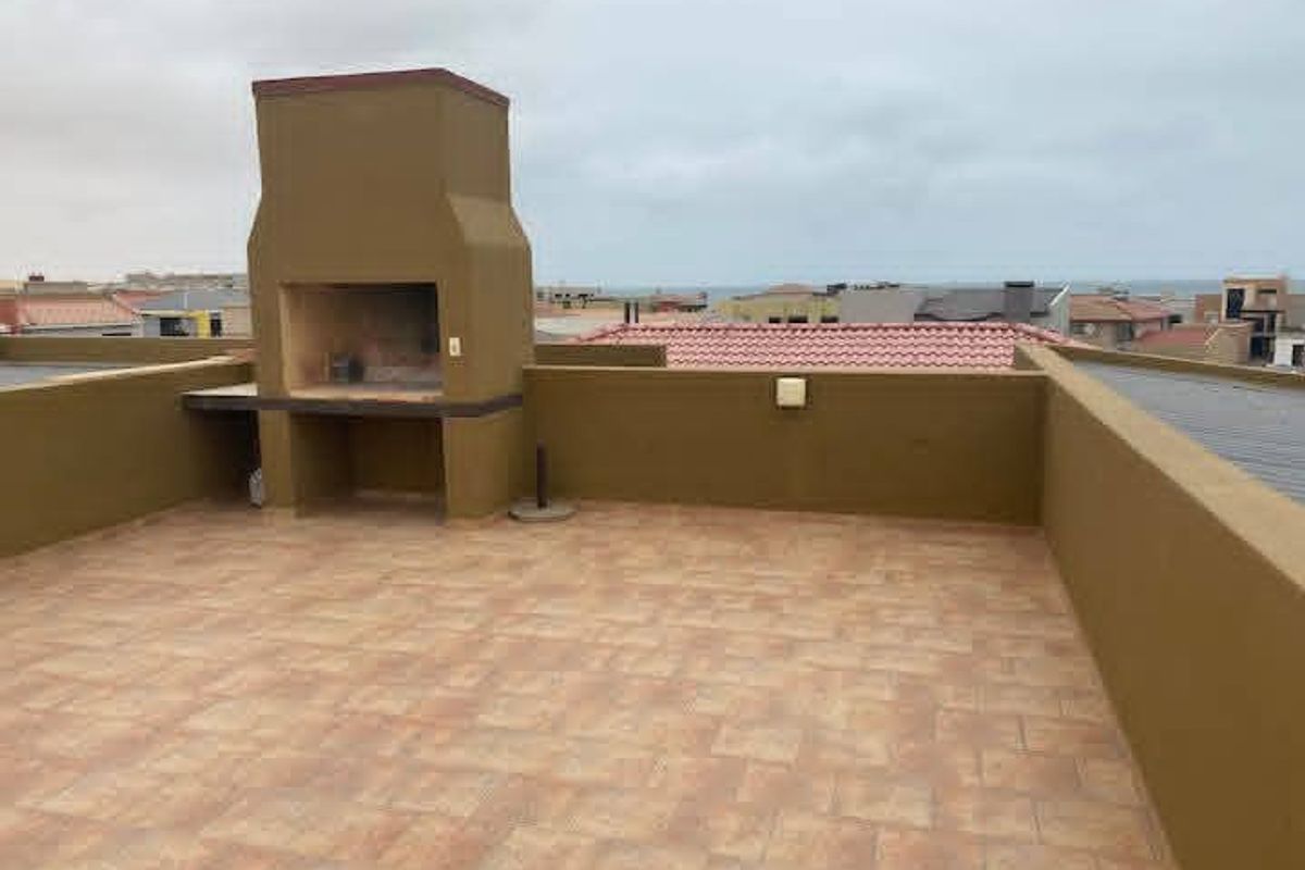 An open-air rooftop patio featuring a built-in braai, tiled flooring, and perimeter walls, offering an elevated outdoor entertainment space.
