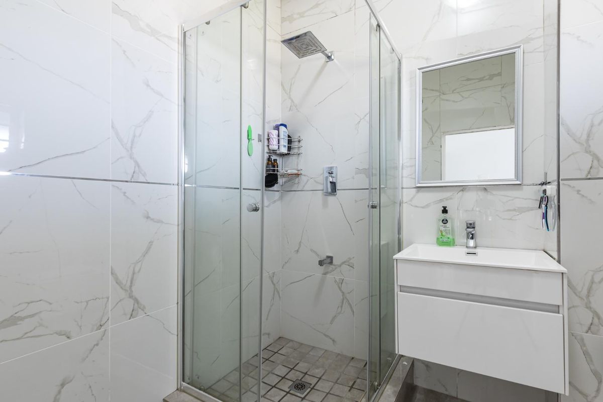Modern bathroom featuring a glass-enclosed shower with rainfall showerhead, marble-look wall tiles, and a wall-mounted vanity unit with a mirror.