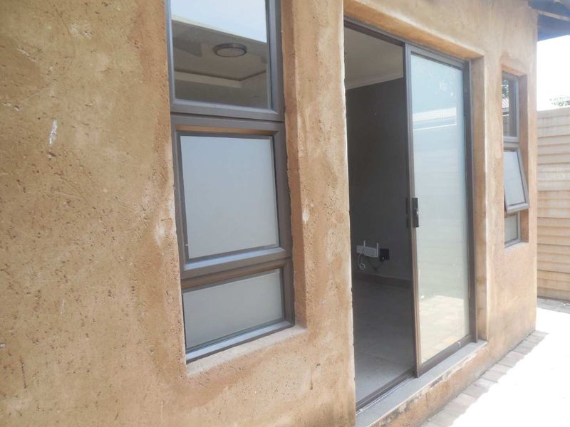 Exterior view of a cottage featuring a sliding glass door, aluminium window frames, and a textured plaster wall finish with a paved walkway.
