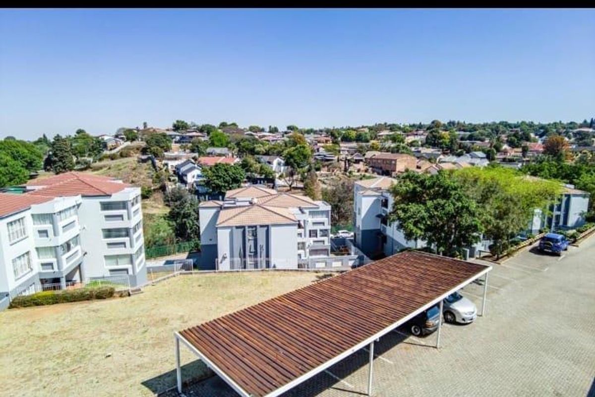 Aerial view of the apartment complex featuring a covered carport area, paved parking, and surrounding residential neighborhood.