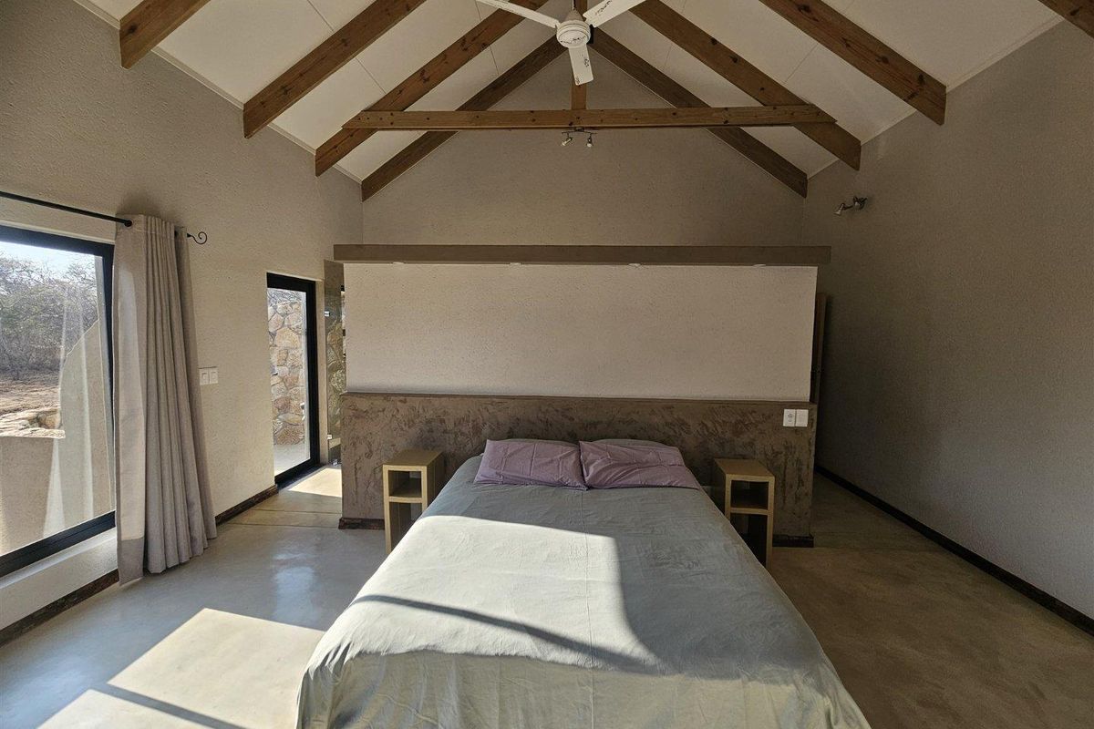 Spacious bedroom featuring high vaulted ceilings with exposed timber trusses, polished concrete floors, and a unique built-in headboard partition with direct outdoor access.