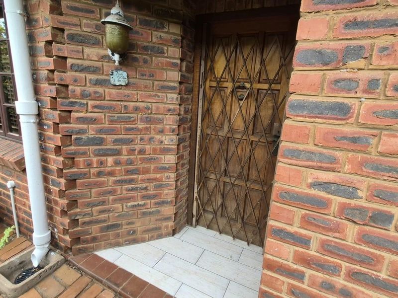 Front entrance featuring a timber door with a security gate, set within a face brick facade with visible masonry cracking.