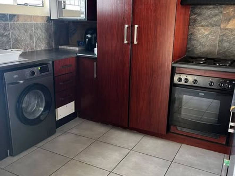 A functional kitchen featuring dark wood-finish cabinetry, built-in oven with hob, extractor fan, tiled backsplash, and tiled flooring.