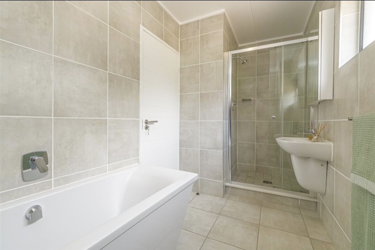 Modern bathroom featuring a separate shower enclosure, bathtub, and wall-mounted basin with neutral floor-to-ceiling tiling.