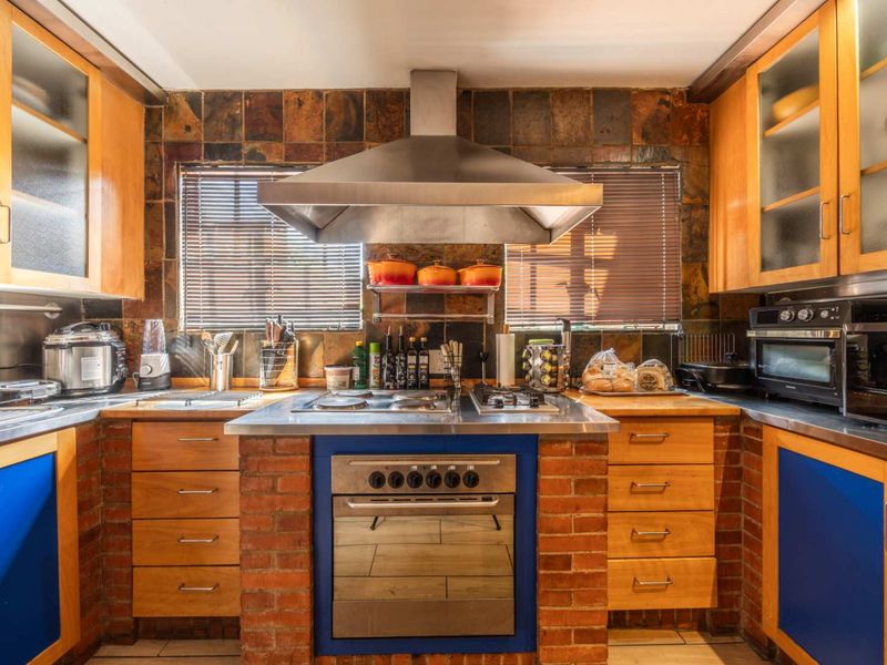 A functional kitchen featuring wooden cabinetry, stainless steel countertops, a built-in oven with gas hob, and a distinctive stone tile backsplash.