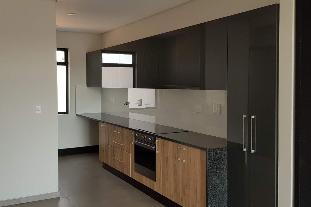 Modern kitchen featuring sleek dark grey and wood-grain cabinetry, stone countertops, integrated oven, and hob with a clean glass splashback.